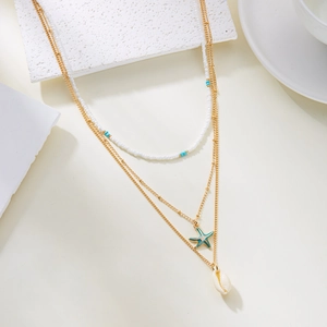 Détail d'un collier doré multicouche avec perles blanches, étoile de mer et coquillage