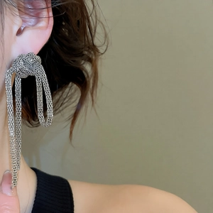 Detail of silver chain knot earrings featuring long woven mesh tassels on model