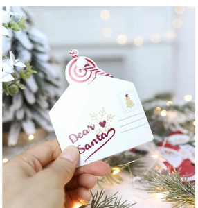 Close-up of Dear Santa envelope gift tag with red twine against Christmas tree lights