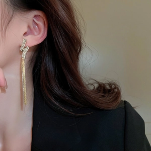 Macro detail of long gold tassel earrings with glittering rhinestones worn by a model