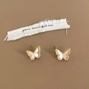Detailed close-up of golden butterfly studs with white shell inlay and zircon accents