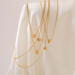 Detailed view of assorted gold bubble letter necklaces draped over white silk fabric