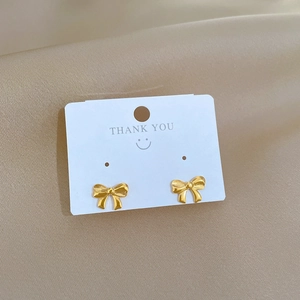 Minimalist gold bow stud earrings in titanium steel displayed on a white gift card