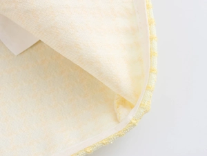 Detailed macro view of the yellow tweed fabric texture and braided edge of the jacket