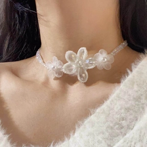 Close-up of a white chiffon flower choker necklace with woven beads worn by a model