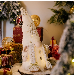 Close-up of glowing plush Christmas gnome with long beard on snowy wooden base