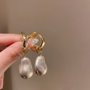 Macro shot of gold irregular metal earrings with baroque pearl charms held by hand