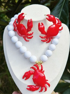 Dettaglio di un set collana e orecchini a forma di granchio rosso su espositore bianco.