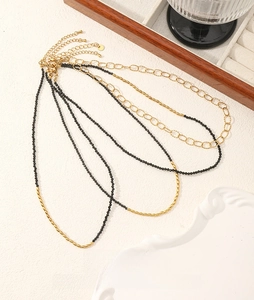 Close-up of black spinel beaded necklaces and gold chains on a white textured background