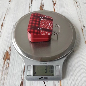 Detail showing red plaid Christmas tin suitcase on a scale weighing 31.0 grams