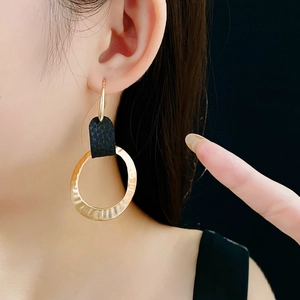 Close-up of textured golden hoop earrings with black leather inlay worn on model