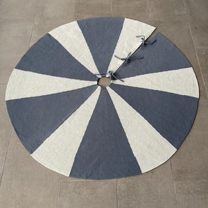 Close-up of blue and off-white knitted Christmas tree skirt with ties on grey floor