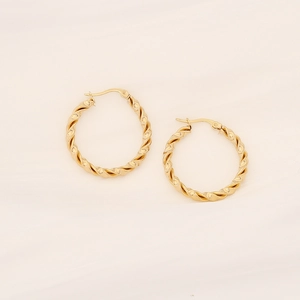 Detailed macro shot of golden twisted texture C-shape earrings on white fabric