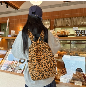 Close-up of stylish leopard print corduroy backpack on a woman in a cozy cafe setting