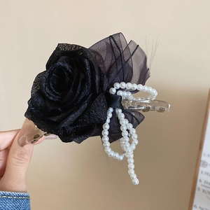 Dettaglio di elegante pinza per capelli con fiore in pizzo nero e nappe di perle