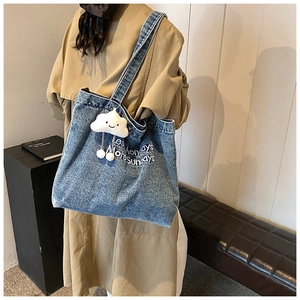 Detail of blue denim tote bag with white embroidery and a cute cloud plush charm