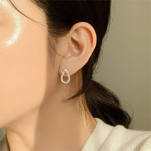 Close-up of polished silver knot earrings worn by a model against a soft beige backdrop