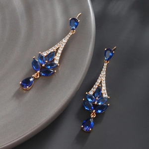 Close-up of geometric blue marquise gems on gold-plated earrings over a dark plate