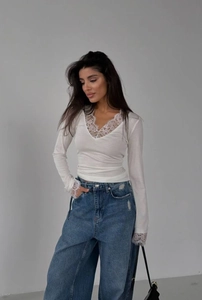 Close-up of elegant lace stitching on the neckline and cuffs of a white slim-fit top