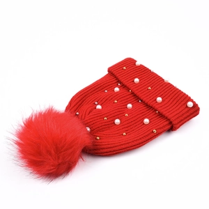 Dettaglio del berretto rosso in maglia con perle bianche e pompon in finta pelliccia