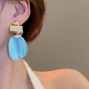 Detail of irregular golden metal piece and large sky blue resin oval drop earring