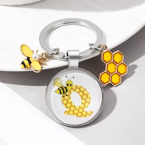 Macro detail of silver keychain with bee charms and letter Q glass dome pendant