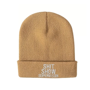 Detail of the white SHIT SHOW SUPERVISOR embroidery on a khaki knitted beanie hat