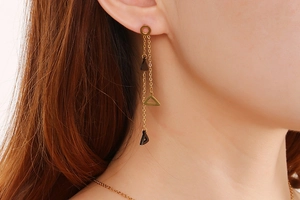 Detailed view of long gold tassel earrings with black and gold triangular charms on a model