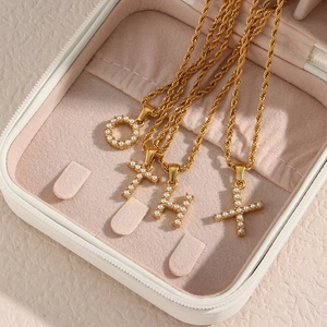 Close-up of 18K gold-plated twist chain necklaces with pearl initial pendants on velvet