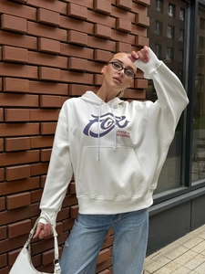 Close-up of white hoodie with blue FOX print and kangaroo pocket against brick wall
