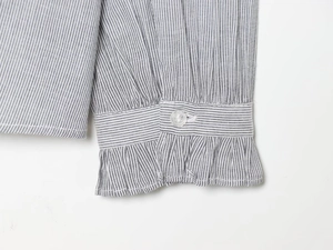 Detail of grey striped shirt cuff with ruffled edges and a clear round button