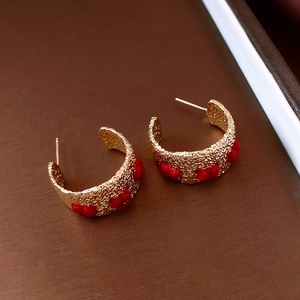 Detail of vintage C-shaped gold earrings with textured finish and red thread weaving