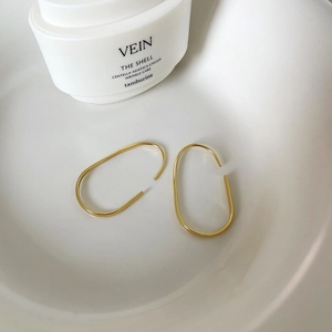 Macro shot of minimalist gold U-shaped oval hoop earrings in a modern ceramic dish