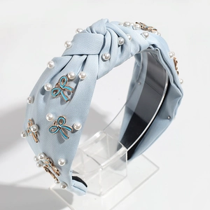 Detail of light blue fabric headband with knotted design, white pearls, and enamel bows