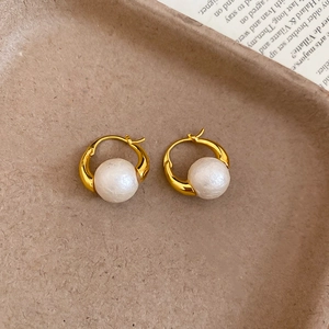Close-up of vintage gold hoop earrings with white pearls on a textured background
