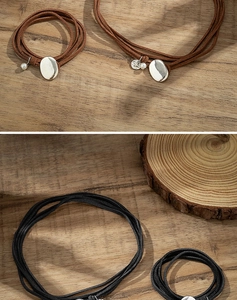Close-up of layered suede choker necklaces in brown and black with silver charms on wood