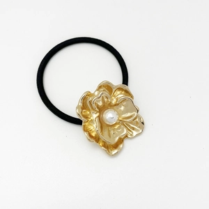 Detail of a black elastic hair tie featuring a golden metal flower with a white pearl center