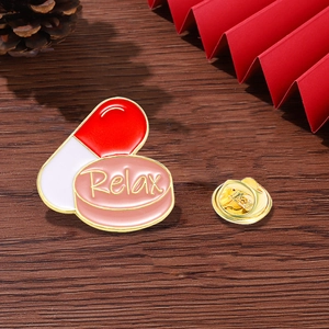 Cartoon pill brooch with Relax text engraving on dark wood background with butterfly pin