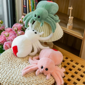 Three colorful plush spiders with heart patterns and big eyes on a woven cushion