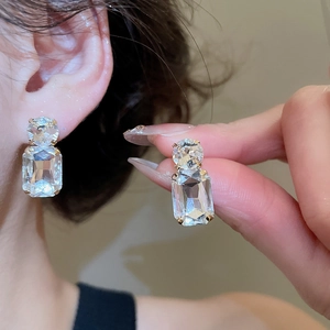 Macro view of geometric crystal earrings with round and emerald cut stones in gold setting