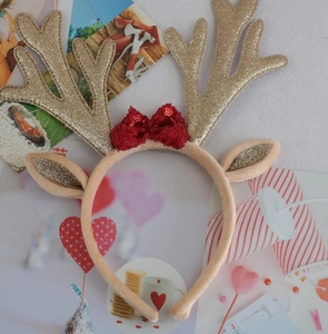 Top view of beige plush Christmas headband with glittery antlers and a red sequin bow
