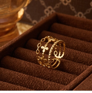 Macro shot of gold layered ring with clover and chain details on brown velvet cushion