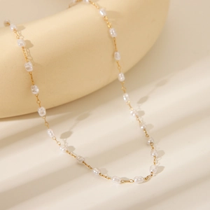 Detailed close-up of 18K gold plated chain with irregular white pearls on a beige surface