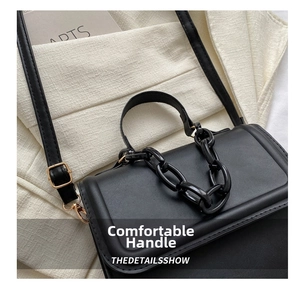Detail of black faux leather bag with chunky chain decor and gold hardware