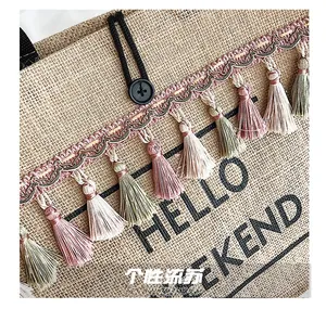 Close-up of jute tote bag showing colorful tassels and Hello Weekend print detail