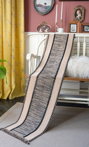 Detail shot of black and beige woven table runner with decorative tassels on a white bench