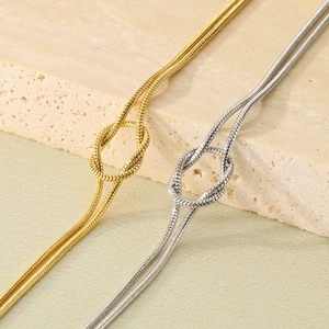 Close-up of gold and silver knot snake chain bracelets on a textured stone surface