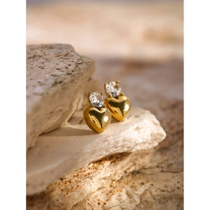 Detail of 18k gold heart studs with white zircon inlay on natural beige stone