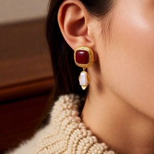 Close-up of vintage gold earrings with deep red square resin and elegant white pearl drop