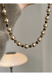 Détail d'un collier vintage avec pierres oeil de tigre et perles champagne sur un pull